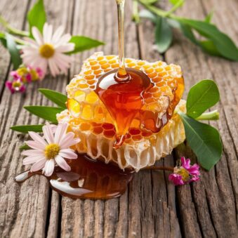 Honey dripping from a honeycomb piece on a wooden surface with fresh flowers and green leaves